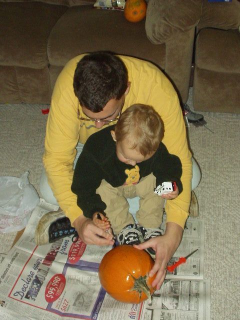 Daddy and Elijah are drawing a face on the pumpkin.