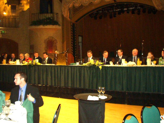 Bruce is sitting by the lady in the red jacket :)