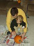 Daddy and Elijah are drawing a face on the pumpkin.